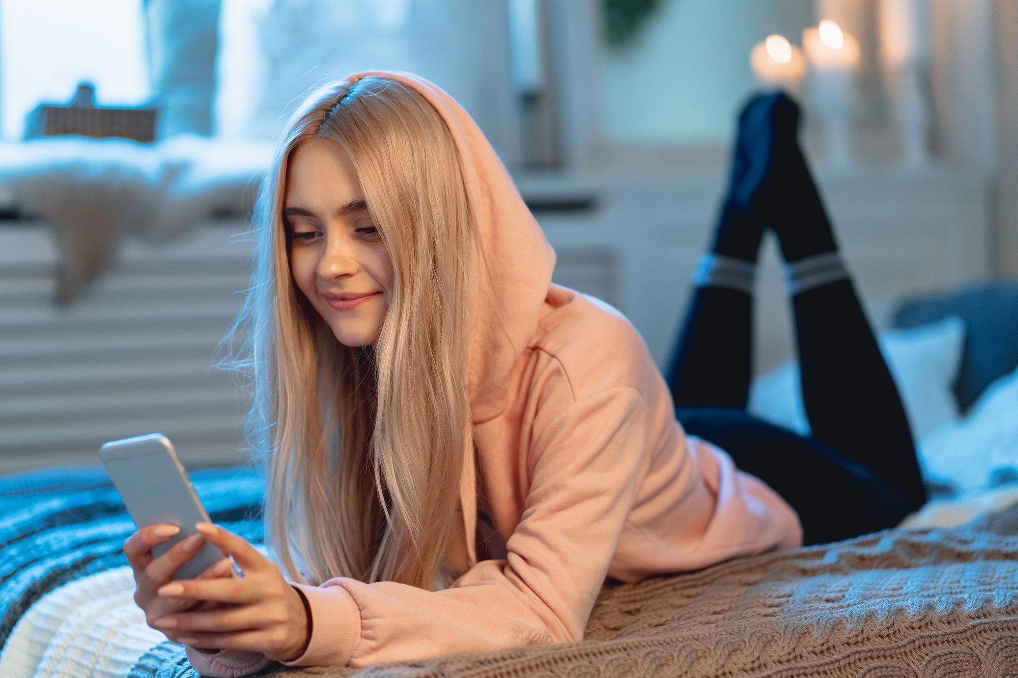 Pretty blond girl in pink using a smart phone lying on the bed a